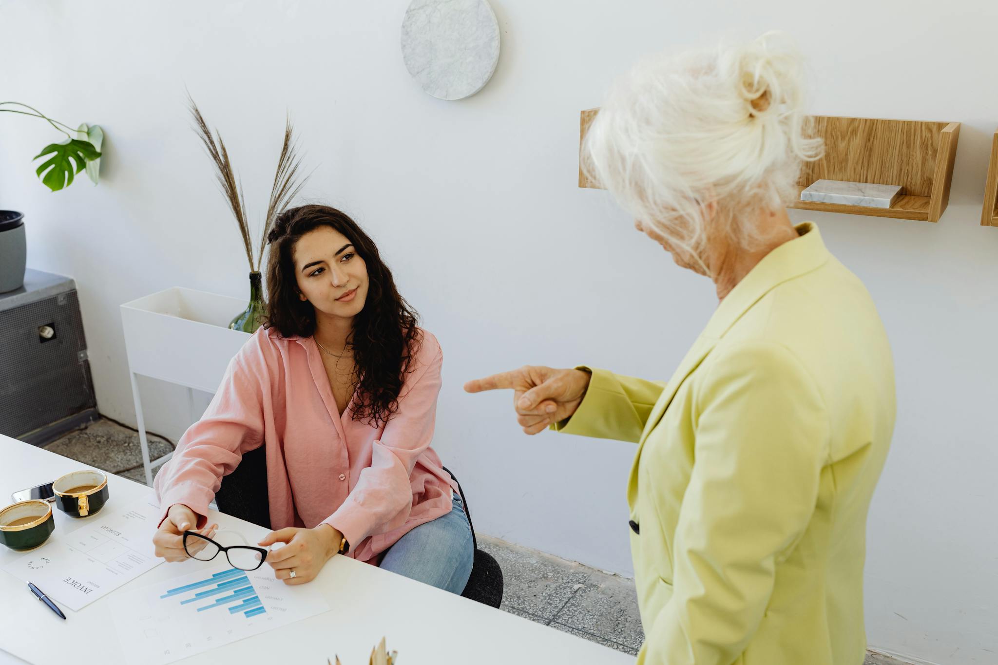 A senior woman in leadership discussing with a young businesswoman at a modern office desk.